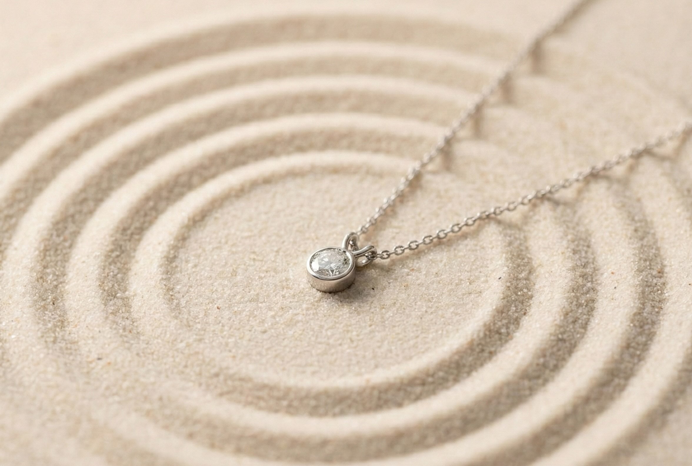 facetsn bezel-set lab-grown diamond pendant necklace in platinum resting on concentric sand circles
