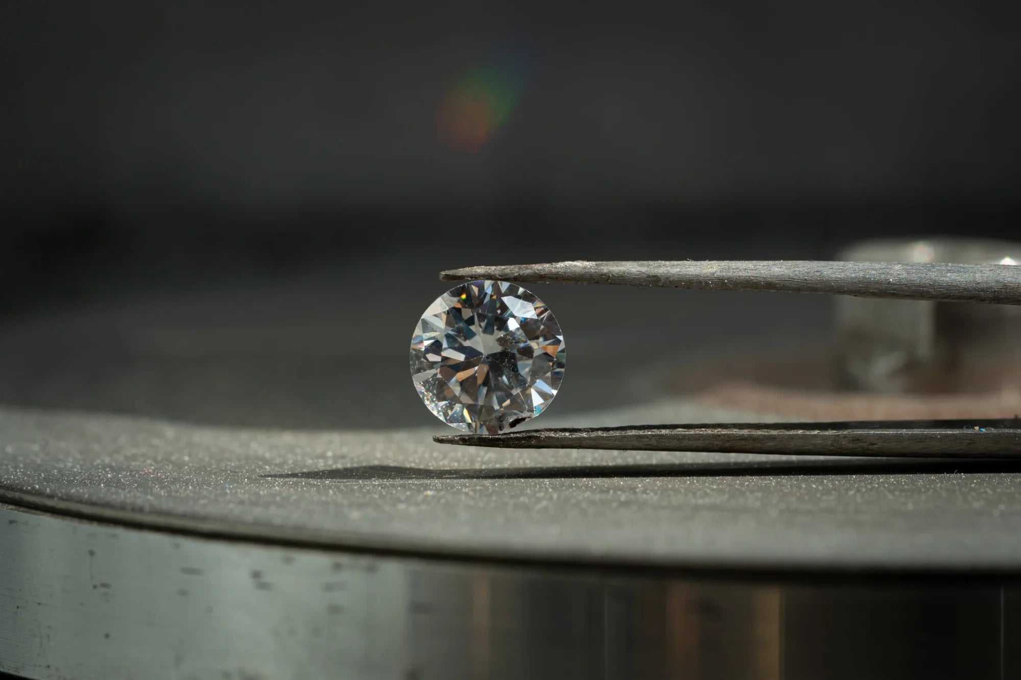 Round brilliant lab-grown diamond on polishing wheel, held by tweezers